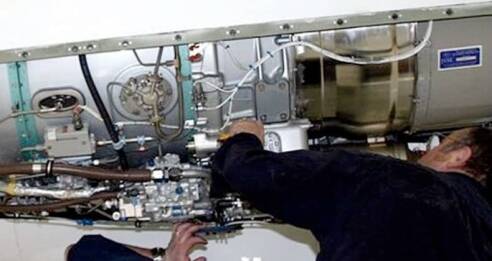 A person is inspecting and working on the internal machinery of an aircraft or industrial equipment, surrounded by complex pipes, wires, and metal components—demonstrating Lean Manufacturing Consulting in action.
