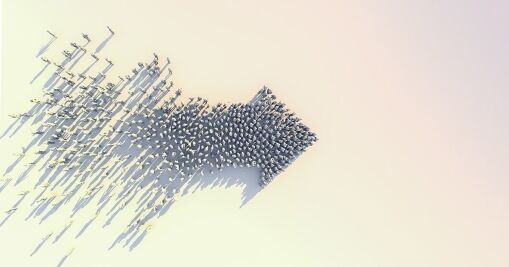 A group of small human figures is arranged to form a large right-pointing arrow, casting long shadows on a light, neutral background. The figures are more densely packed at the arrowhead, and more spaced out at the tail.