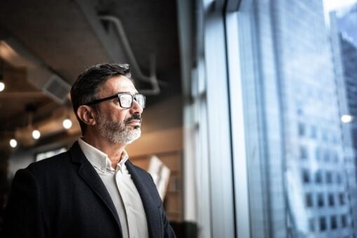 Business leader looking out office window, reflecting on vision and leading organizational change.