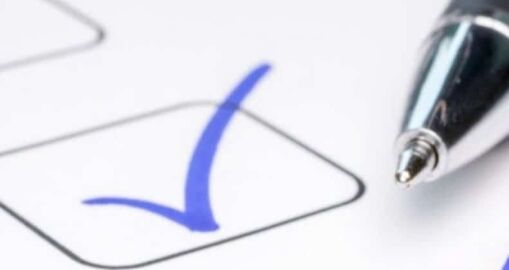 A close-up of a pen next to a checkbox on paper, with a blue checkmark inside the box.