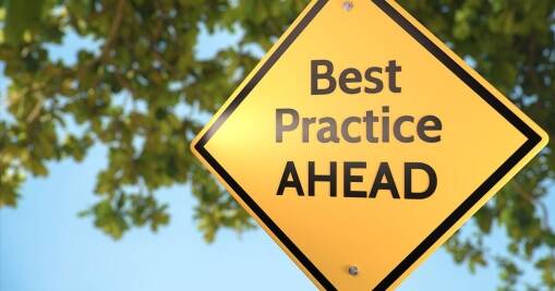 A yellow diamond-shaped road sign reads Best Practice AHEAD with green tree branches and a blue sky in the blurred background.