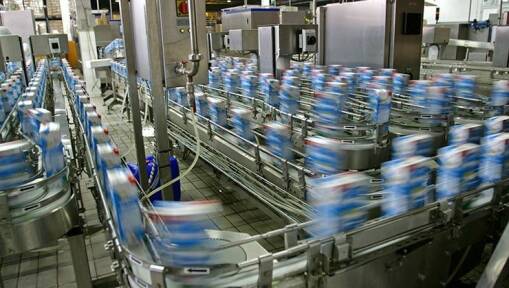 Automated conveyor belts in a factory move rows of blurred cartons, likely milk or juice, quickly through a production line surrounded by stainless steel machinery.