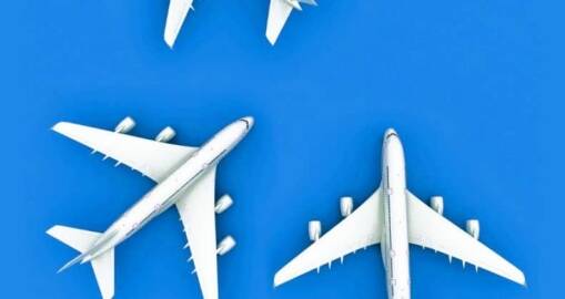 Three white passenger airplanes are positioned on a bright blue background, viewed from above. Two planes are facing left and right, while the third is oriented upward.